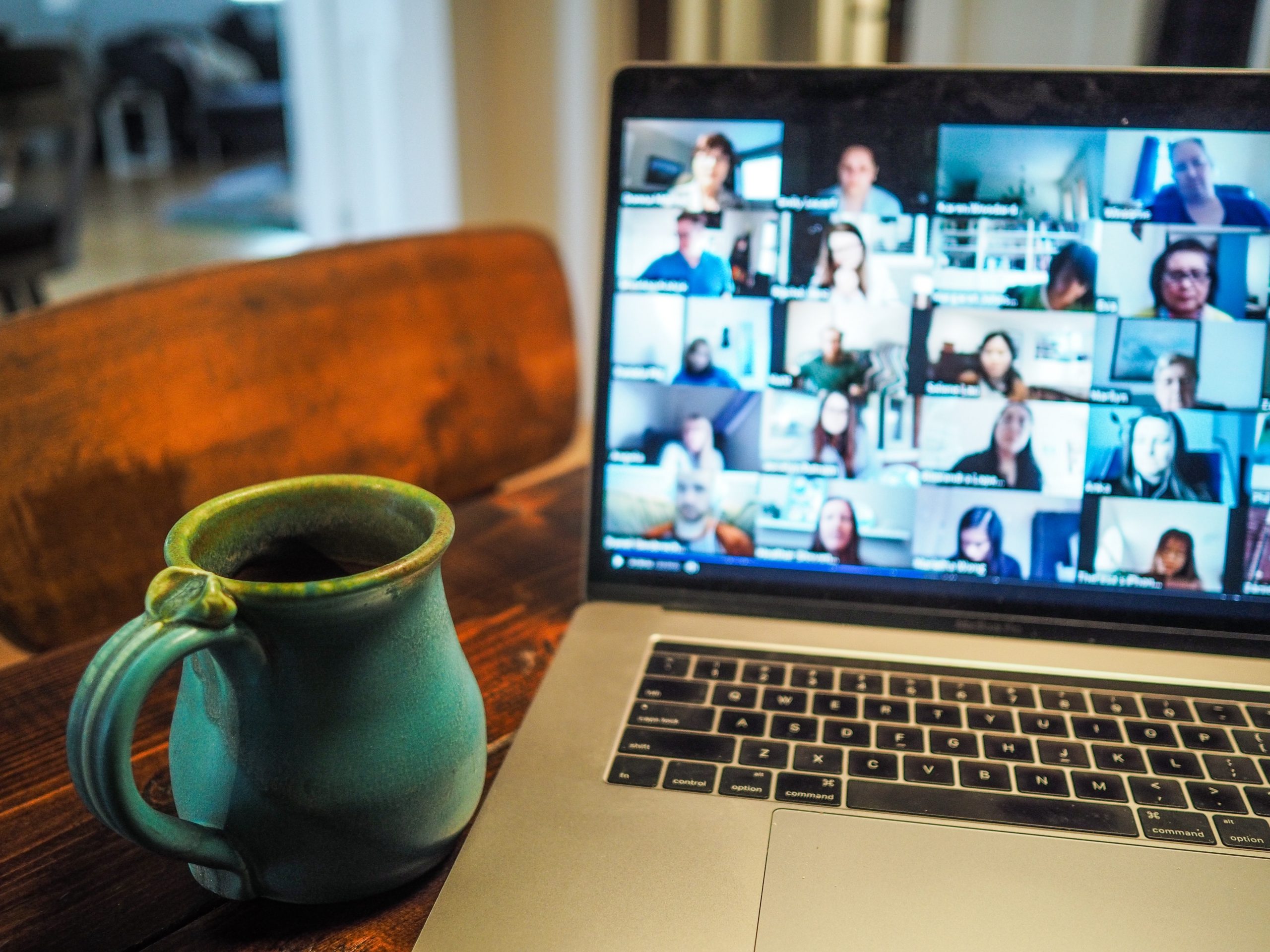 laptop on table with computer screen open to Zoom call or online classroom. Cup of coffee on table.