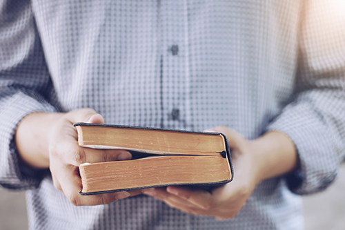 person in button-up shirt holding a book that looks like a Bible