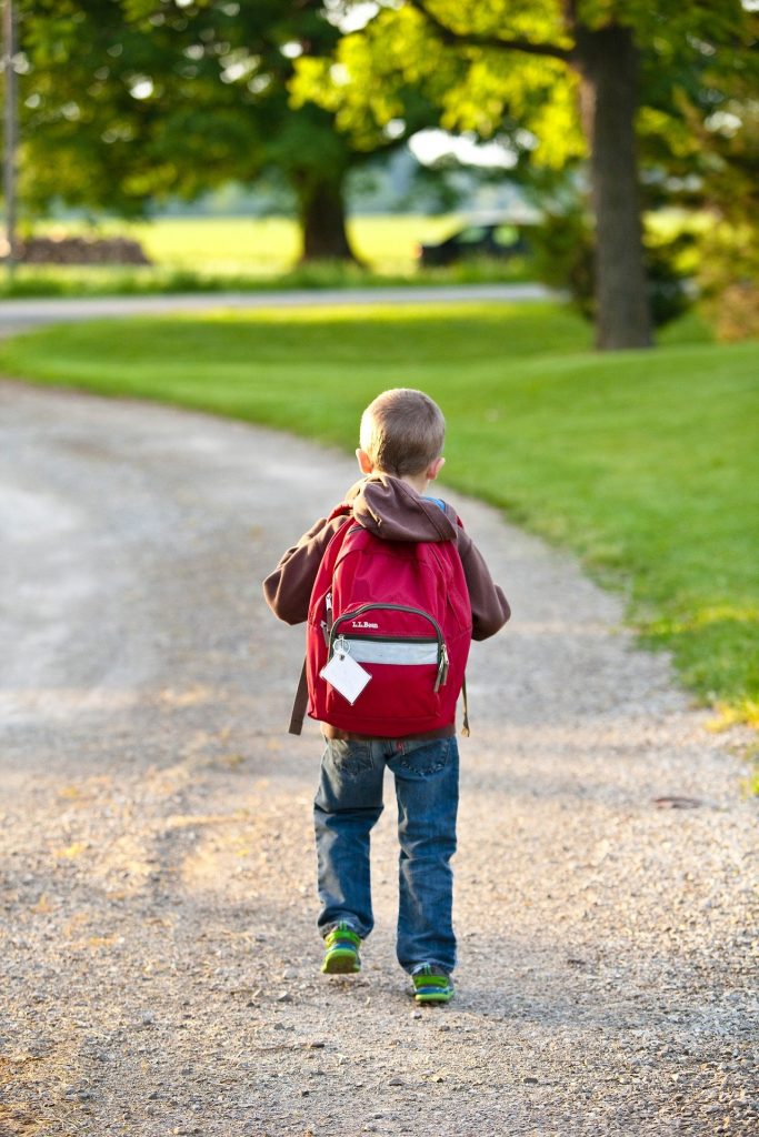 young boy with school backpack walking down gravel road