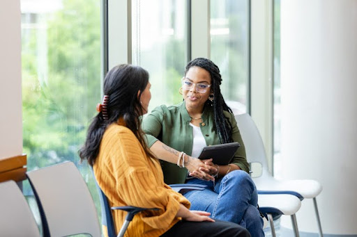 A counselor and a client sitting in chairs next to a window in a room.