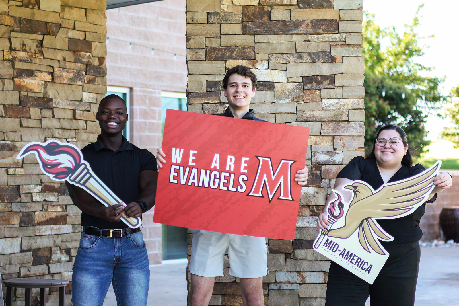 Three students standing together holding MACU signs.