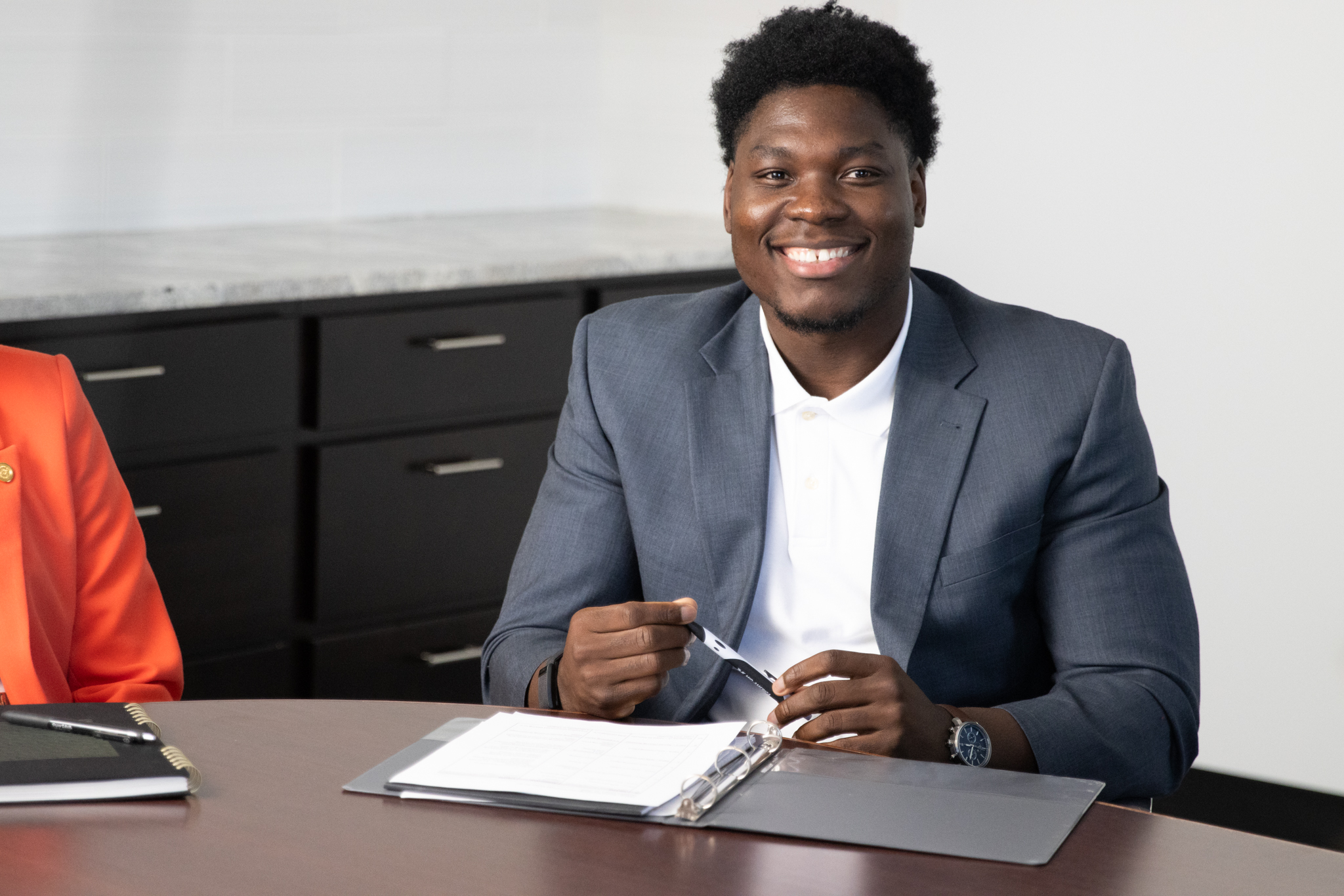 A male MACU student in business attire sits at a conference table.