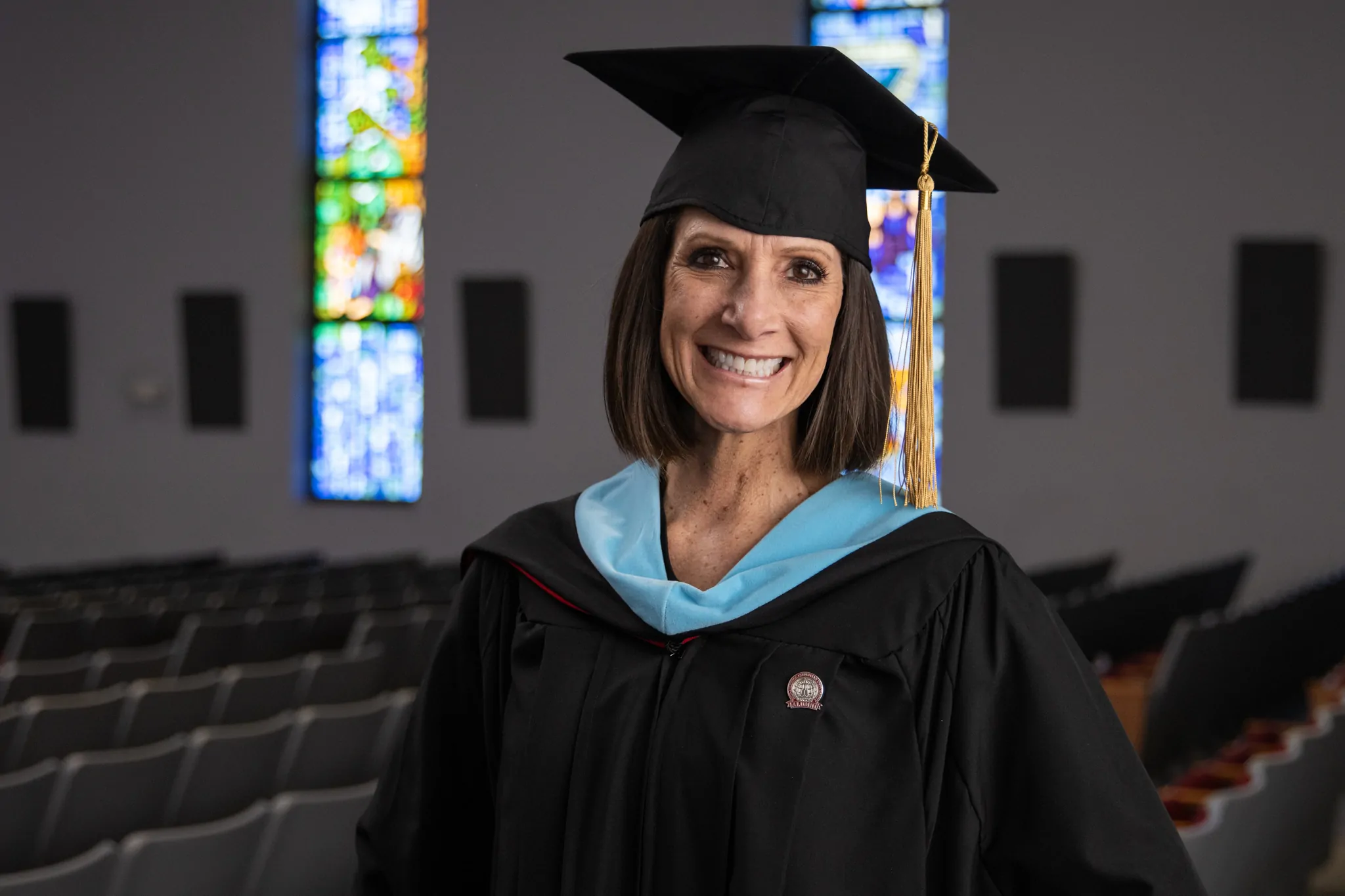 A female graduate wearing a cap and gown stands in the MACU Chapel.