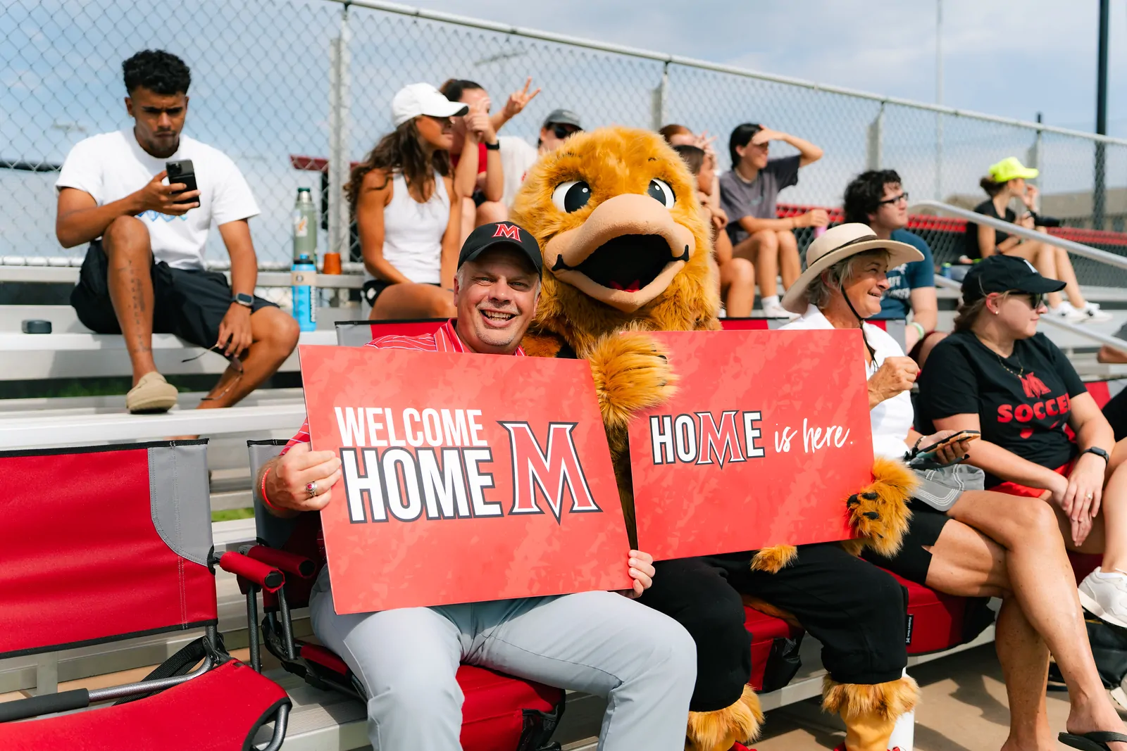 President Greenwald sits with mascot Max the Evangel at a baseball game.