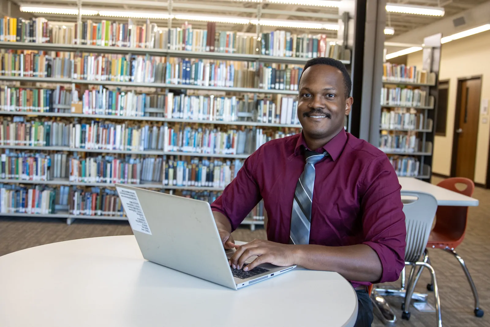 A cybersecurity student uses a laptop computer in the MACU library.