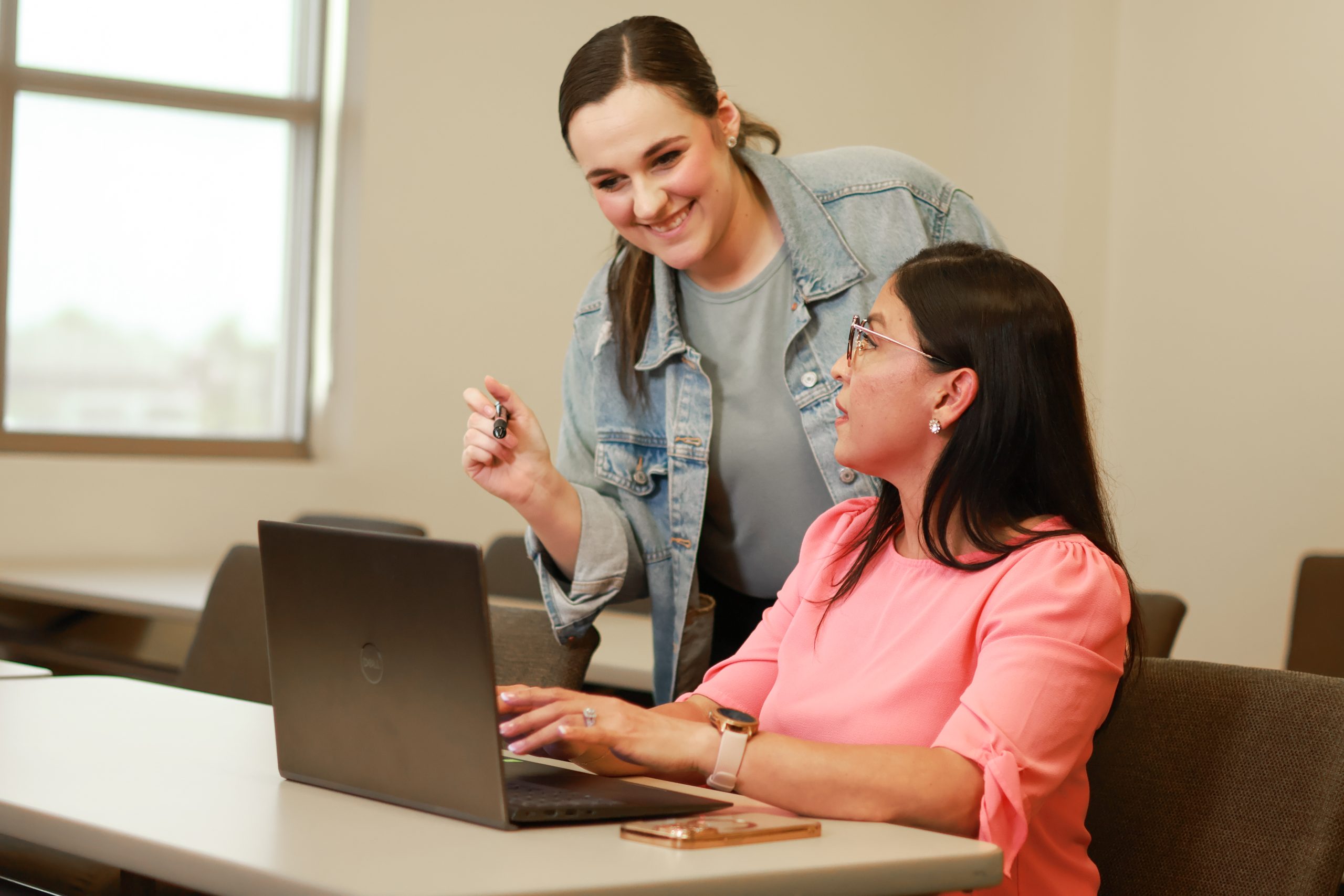 Two female students speak in a college classroom.
